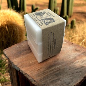 Peut inclure: Trois savons au lait de chèvre blancs enveloppés de papier brun avec le texte "Happy Soul Organics" et "Face Unscented 1.5 oz GOAT MILK SOAP" imprimé sur l'étiquette. L'étiquette indique également les ingrédients : "lait de chèvre, tocznat biologique" et le site Web "www.HappySoulOrganics.com".