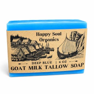 May include: A rectangular bar of bright blue goat milk tallow soap wrapped in a tan paper label. The label features black ink illustrations of a Viking village and a longship, with the text Happy Soul Organics, Deep Blue, 4 oz, and Goat Milk Tallow Soap.