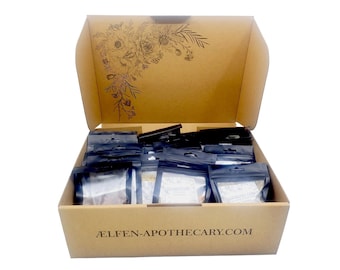 Puede incluir: Una caja de cartón abierta llena de pequeños paquetes sellados. La caja tiene un diseño floral en el interior de la tapa y el texto "ÆLFEN-APOTHECARY.COM" en la parte delantera. Los paquetes son negros y blancos.