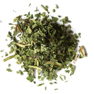 May include: A small, centered pile of dried green herbs consisting of fragmented leaves and thin, woody stems. The texture is coarse and varied, featuring shades of dark and light forest green, with some pieces appearing slightly brownish or tan.