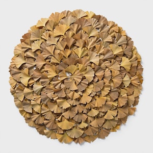 May include: A circular wall art piece composed of numerous dried, fan-shaped ginkgo biloba leaves arranged in a dense, overlapping radial pattern. The leaves display natural shades of muted tan, beige, and light brown throughout the display.