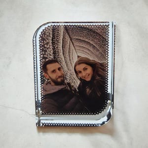 May include: A rectangular glass block featuring a laser-etched black and white photograph of two people. The image shows a person with a beard and a person with long hair standing in front of a tunnel of lights. The glass has a bevelled edge.