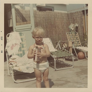 May include: A vintage photograph of a young child in a swimsuit holding a box. The child is standing on a concrete patio, with beach chairs and a basketball in the background. The photo is dated September 1968.