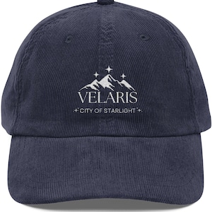 May include: Navy blue corduroy baseball cap with a curved brim. The cap features the white text "VELARIS" above a mountain range graphic, with "+ CITY OF STARLIGHT +" below. A classic, adjustable hat.