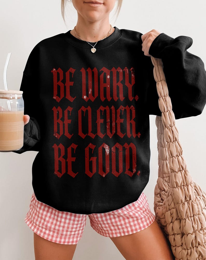 Black sweatshirt with red gothic text "BE WARY. BE CLEVER. BE GOOD."