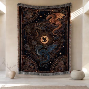 Könnte beinhalten: Eine rechteckige Webdecke mit dunkelblauem Hintergrund und drei Drachen in Gold, Blau und Schwarz. Das Design zeigt ein zentrales Sonnenmotiv mit einer kleinen Drachensilhouette, umgeben von wirbelnden Wolken und Sternen, mit ausgefransten Rändern.