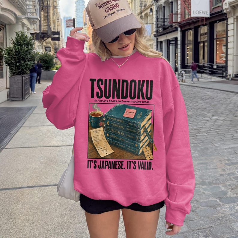 Pink sweatshirt with "TSUNDOKU" and stack of books graphic.