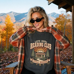 T-shirt graphic with "Late 1900s Reading Club Still Booked" and bookstore illustration.