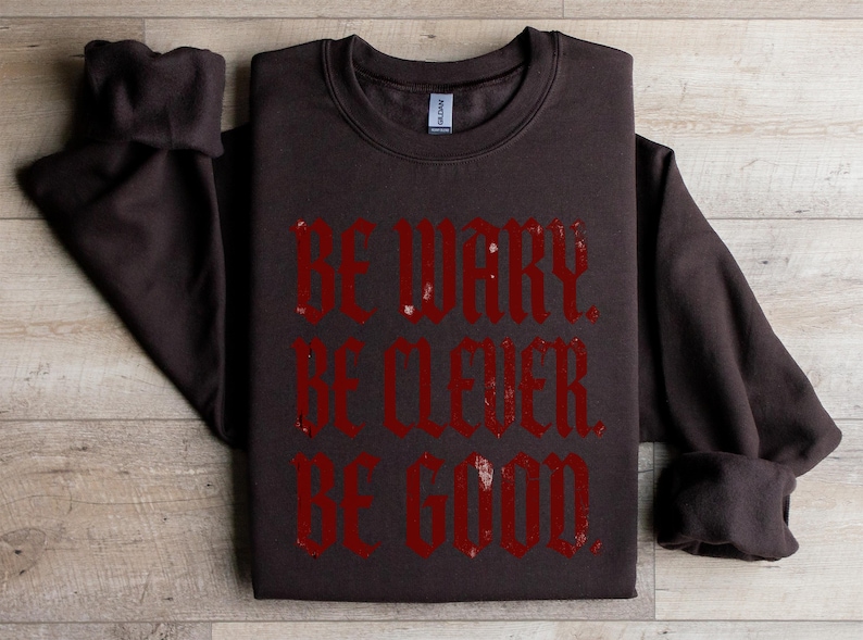 Brown sweatshirt with red text "BE WARY. BE CLEVER. BE GOOD."