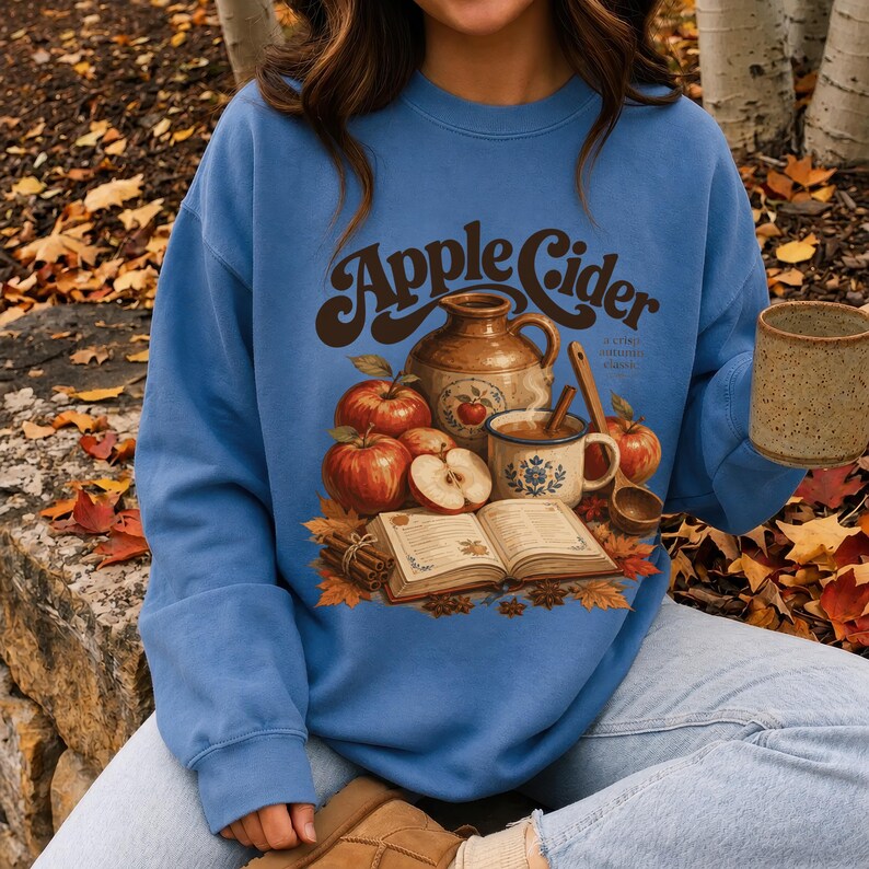 Blue sweatshirt with "Apple Cider a crisp autumn classic" graphic and autumn elements.
