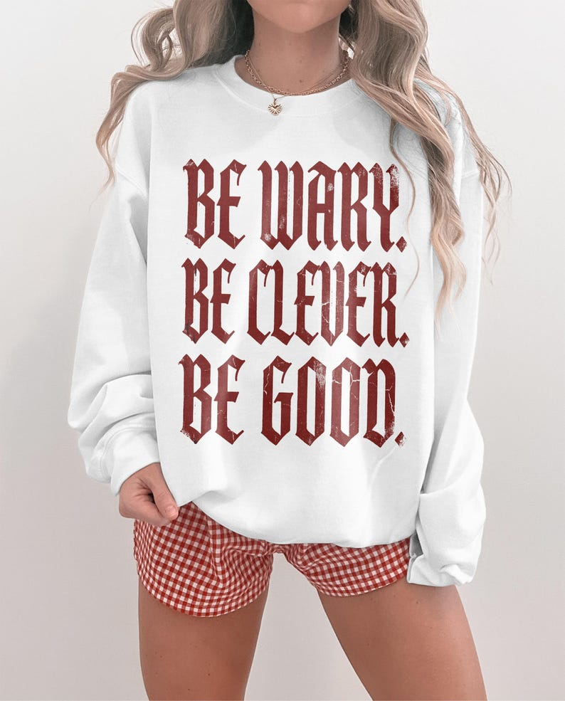 White crewneck sweatshirt with "BE WARY. BE CLEVER. BE GOOD." in gothic font.