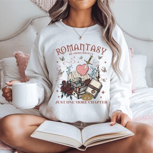a woman sitting on a bed holding a book and a mug