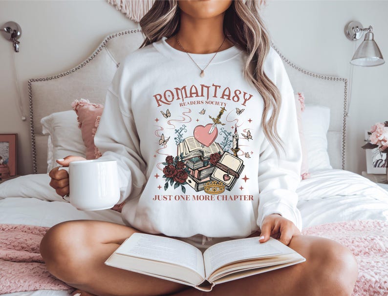 a woman sitting on a bed holding a book and a mug