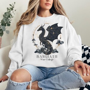 a woman sitting on a couch wearing a white sweatshirt with a black dragon on it