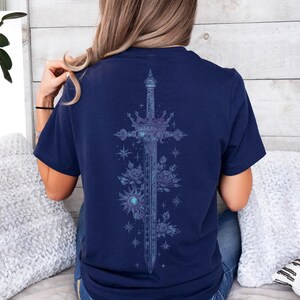 a woman sitting on a bed wearing a t - shirt with a cross on it