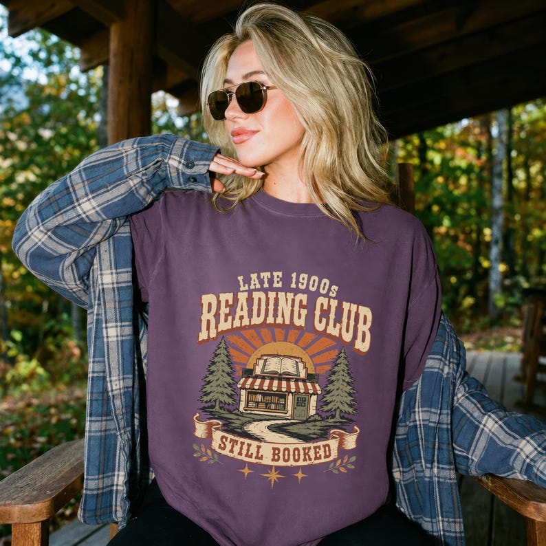 Purple t-shirt with "Late 1900s Reading Club Still Booked" text and bookstore graphic.