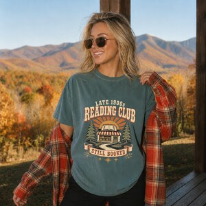 Teal t-shirt with "Late 1900s Reading Club Still Booked" graphic and plaid shirt.