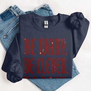 Navy sweatshirt with distressed red text reading "BE WARY. BE CLEVER."