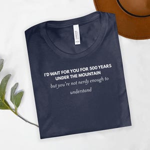 May include: Navy blue t-shirt with the text "I'D WAIT FOR YOU FOR 500 YEARS UNDER THE MOUNTAIN but you're not nerdy enough to understand" in white. The shirt is made of a soft material.