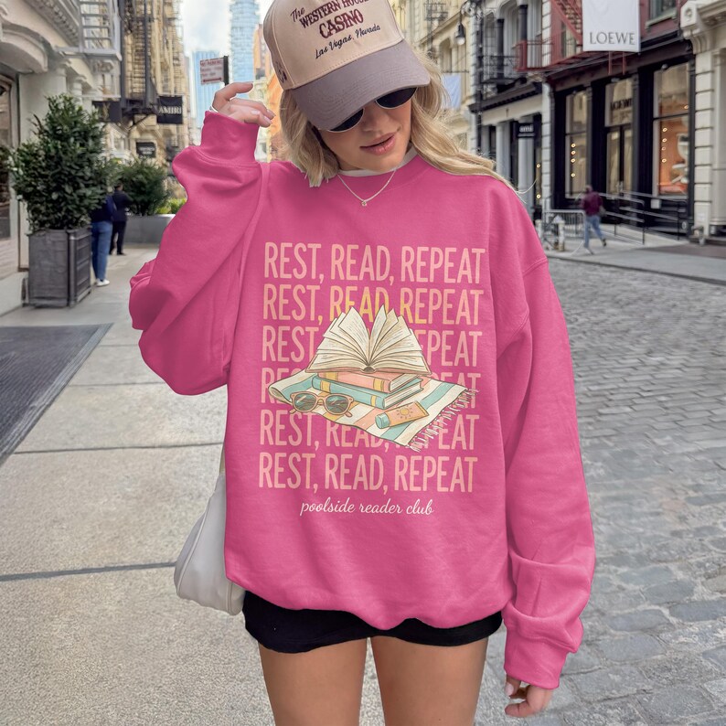Pink sweatshirt with "REST, READ, REPEAT" design featuring an open book.
