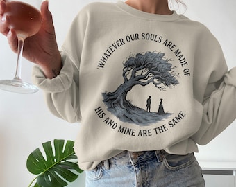 May include: Beige sweatshirt with a graphic of a tree and two figures, with the text "Whatever our souls are made of, his and mine are the same." The sweatshirt is paired with blue jeans.