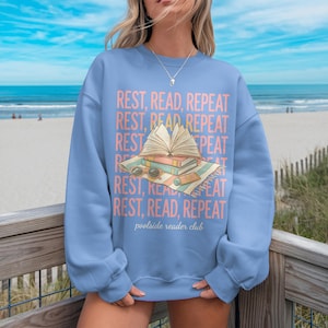 Light blue sweatshirt with "REST, READ, REPEAT" text and book graphic.