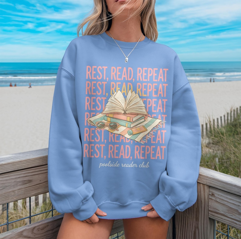 Light blue sweatshirt with "REST, READ, REPEAT" text and book graphic.