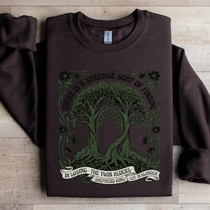 Dark brown sweatshirt with green tree design and text: "There is a strange sort of finding in losing the twin alders. Shepherd King est. in blunder."