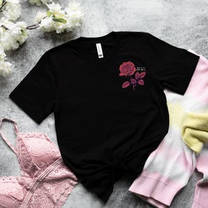 a black t - shirt with a pink rose on it next to a pair of