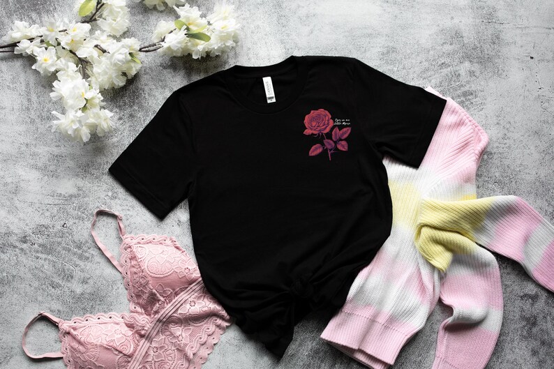 a black t - shirt with a pink rose on it next to a pair of