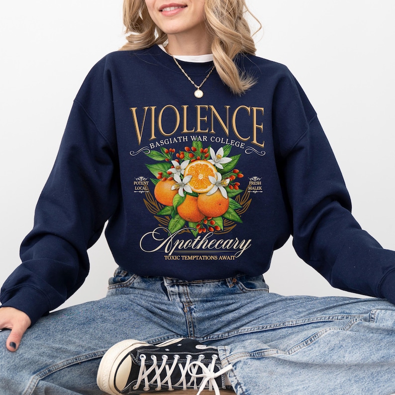 a woman sitting on the ground wearing a sweatshirt with a picture of an orange on