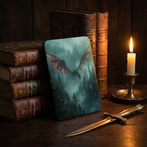 May include: A fantasy-themed phone case featuring a red dragon soaring over a misty forest. The case is displayed with antique books, a candle in a brass holder, and a decorative dagger on a wooden surface.