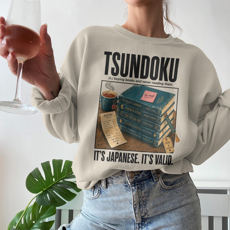 Sweatshirt with "Tsundoku" definition and stacked books, receipt, and "It's Japanese. It's Valid." text.