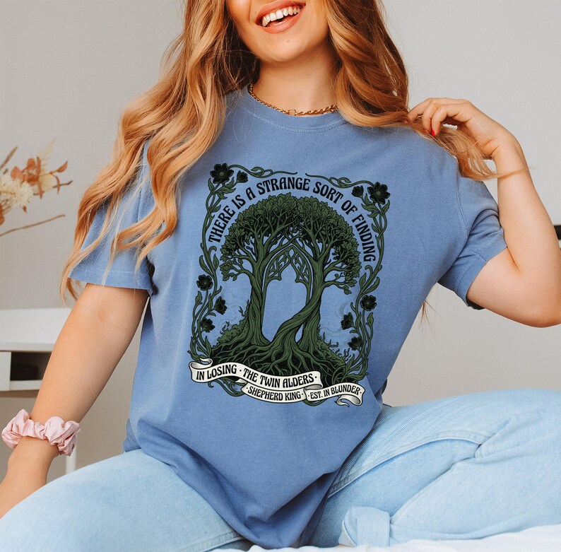 Blue t-shirt with twin trees and text "There is a strange sort of finding in losing".