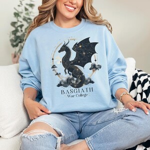 a woman sitting on a couch wearing a blue sweatshirt with a black dragon on it