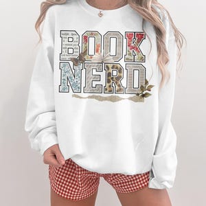 White sweatshirt with "BOOK NERD" graphic in floral and leopard print letters.