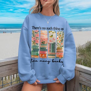 Blue sweatshirt with "There's no such thing as too many books" and floral book stack graphic.