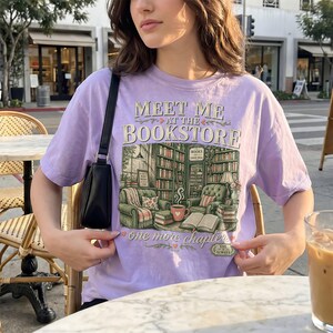 Purple t-shirt with "Meet Me at the Bookstore" and cozy reading nook illustration.