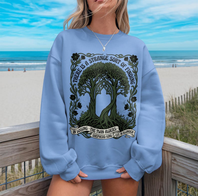 Light blue sweatshirt with ornate tree design and text "There is a strange sort of finding in losing the twin alders."