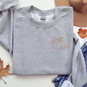 a gray sweater with a pumpkin embroidered on it