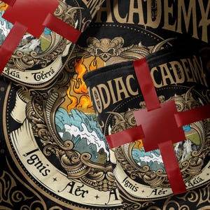 Könnte beinhalten: Schwarzes zylindrisches Produkt mit goldenen und weißen Zierdesigns, rotem Band und dem Text "Zodiac Academy". Das Design umfasst Illustrationen von Feuer, Wasser und Bergen. Das Produkt ist mit einem roten Band umwickelt.