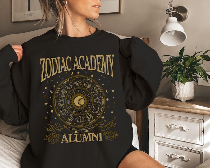 a woman in a black zodiac sweatshirt sitting on a bed