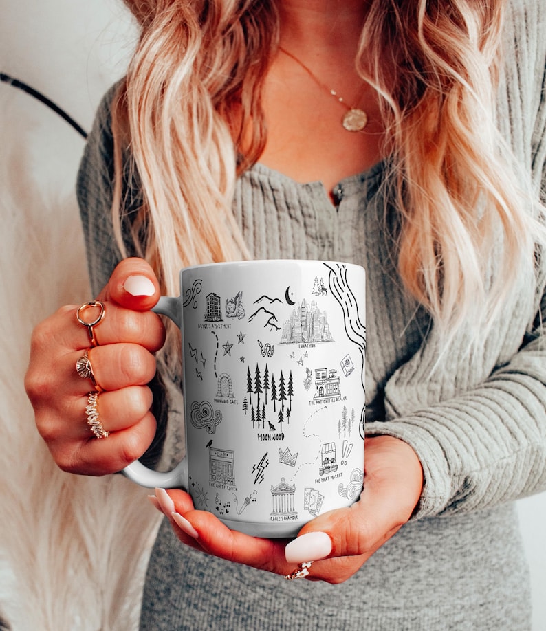 A woman with long blonde hair is holding a mug with various illustrations and text on it.