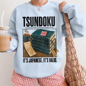 Light blue sweatshirt with "TSUNDOKU" and book stack with receipt.
