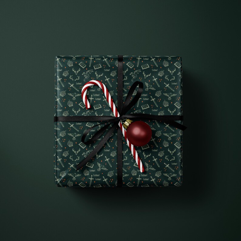 A square gift box wrapped in a dark green patterned paper with a red and white striped ribbon and a red ornament.