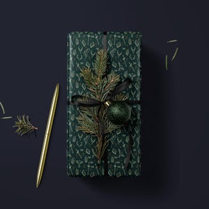 A green gift box with a gold pen and a small green ornament on top, placed on a dark blue background.