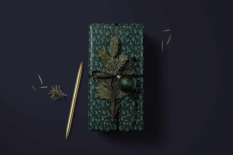 A green gift box with a gold pen and a small green ornament on top, placed on a dark blue background.