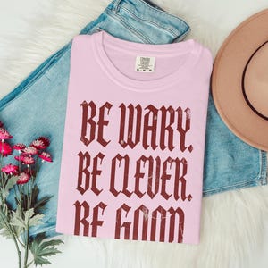 Pink t-shirt with "Be Wary Be Clever Be Good" text.
