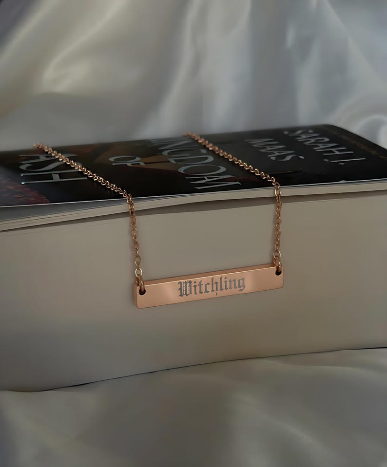 A necklace with a rectangular pendant engraved with the word "Witchling" is resting on top of a book.