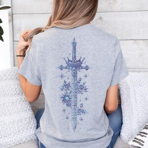 a woman sitting on a bed wearing a t - shirt with a cross on it